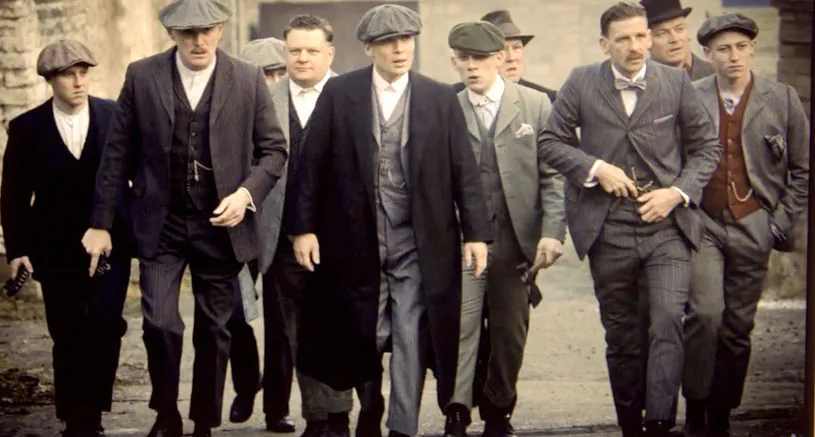 Peaky Blinders characters walking in three-piece suits, overcoats and flat caps.