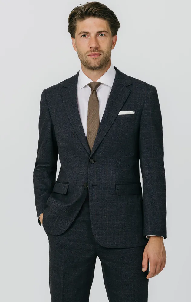 Model wearing a navy suit with a rust check, white shirt and brown tie, suited to a men's smart dress code.