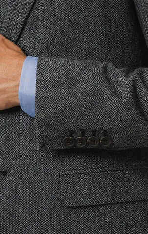 Close-up of a grey herringbone tweed jacket sleeve with four buttons and a light blue shirt cuff.