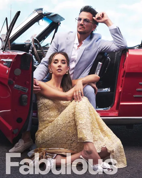 Peter Andre wearing a light blue Dobell suit beside Emily Andre in a red convertible